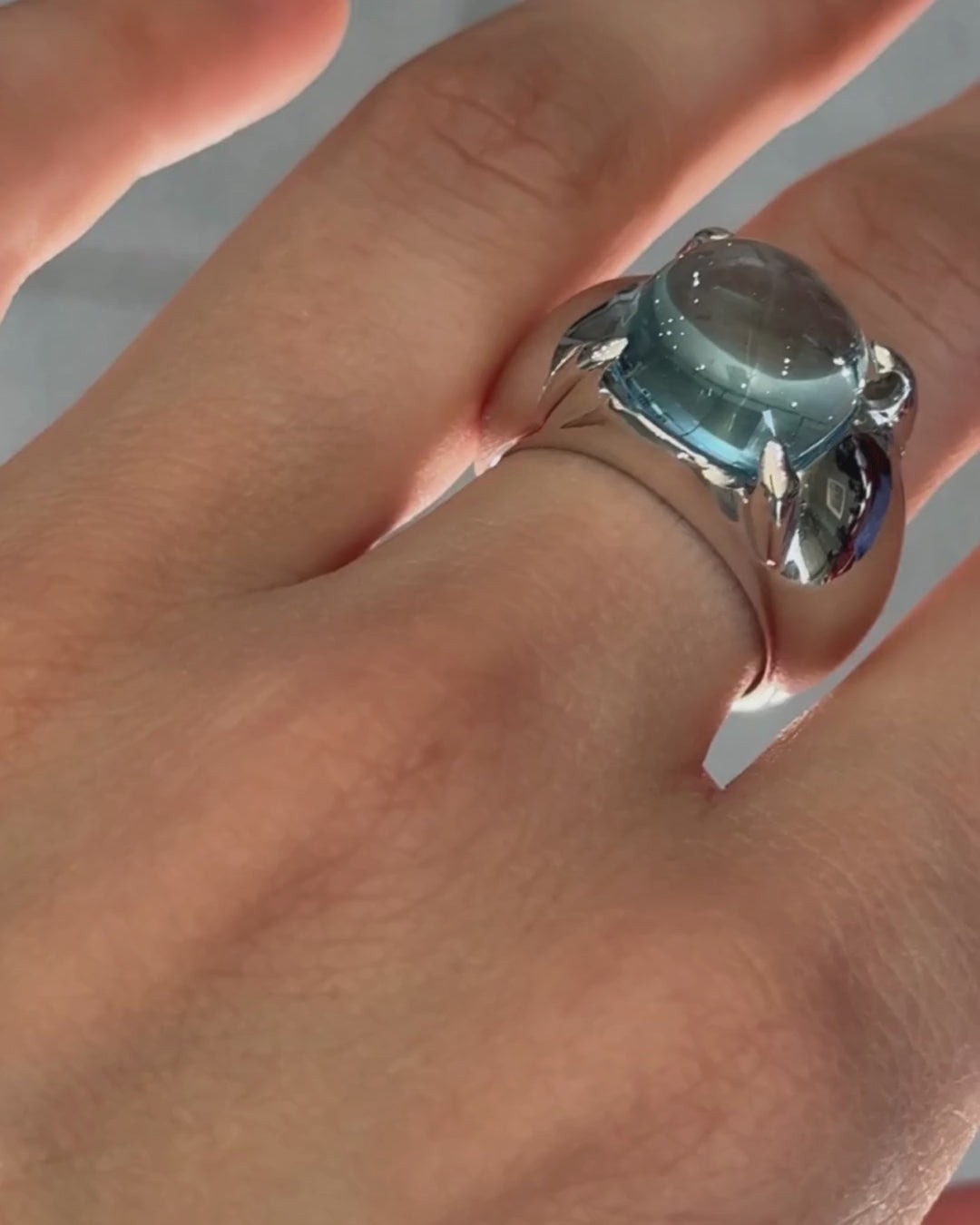 En la imagen se muestra el Anillo Solara, una pieza refinada en plata de ley 925 con acabados en oro amarillo o blanco. La joya centra un topacio natural en cabochón oval, resplandeciente en tonos azul celeste, perfecto para destacar en cualquier evento especial y añadir un toque de elegancia clásic